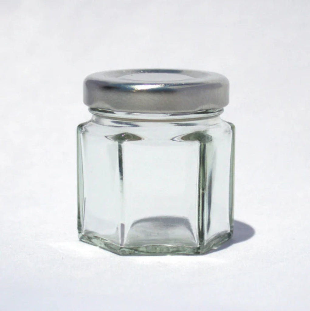 Hexagonal glass jar with a silver lid on a white background