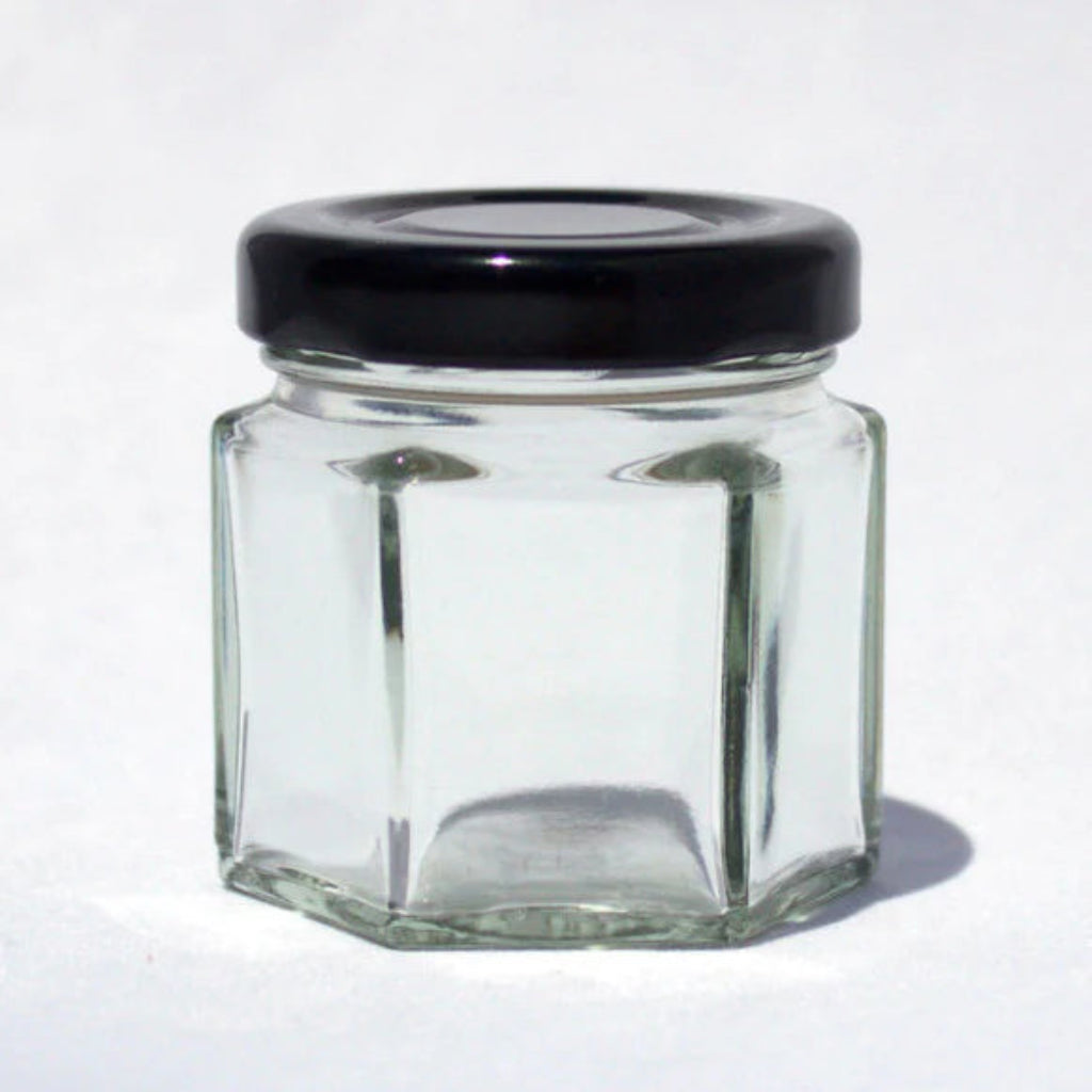 Clear glass hexagonal jar with a black lid on a white background